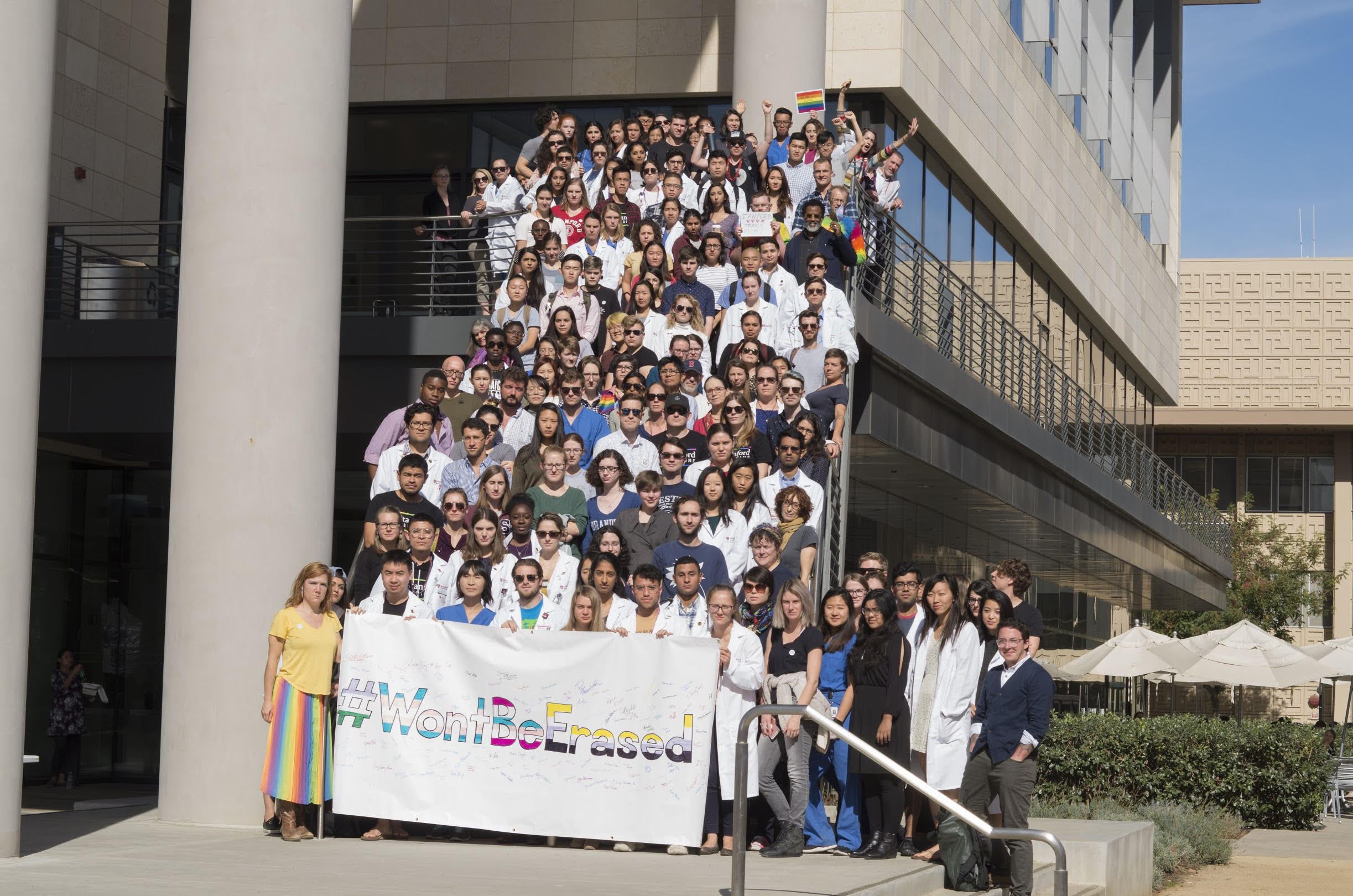 A group of ~100 med students on a staircase, posing with a large banner reading Won't Be Erased.