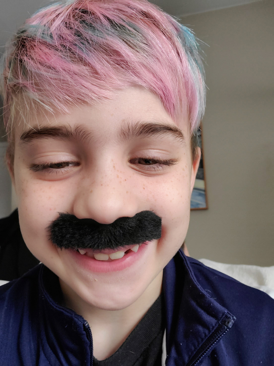 Wade smiling with a large fake mustache on his face. His hair is dyed a mix of cotton candy pink and blue.