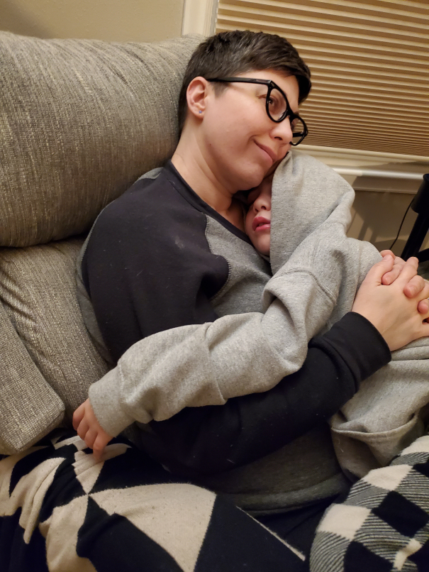 Stephani, a mom who challenged surgery for congenial adrenal hyperplasia, holds her son Wade. The two sleep cozily on a couch with their eyes closed.