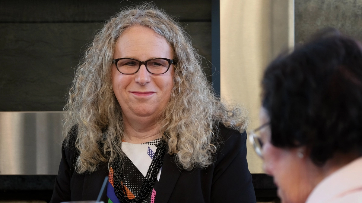 Dr. Rachel Levine faces the camera with a slight smile. She is a white transgender woman with long gray hair and black rimmed glasses.