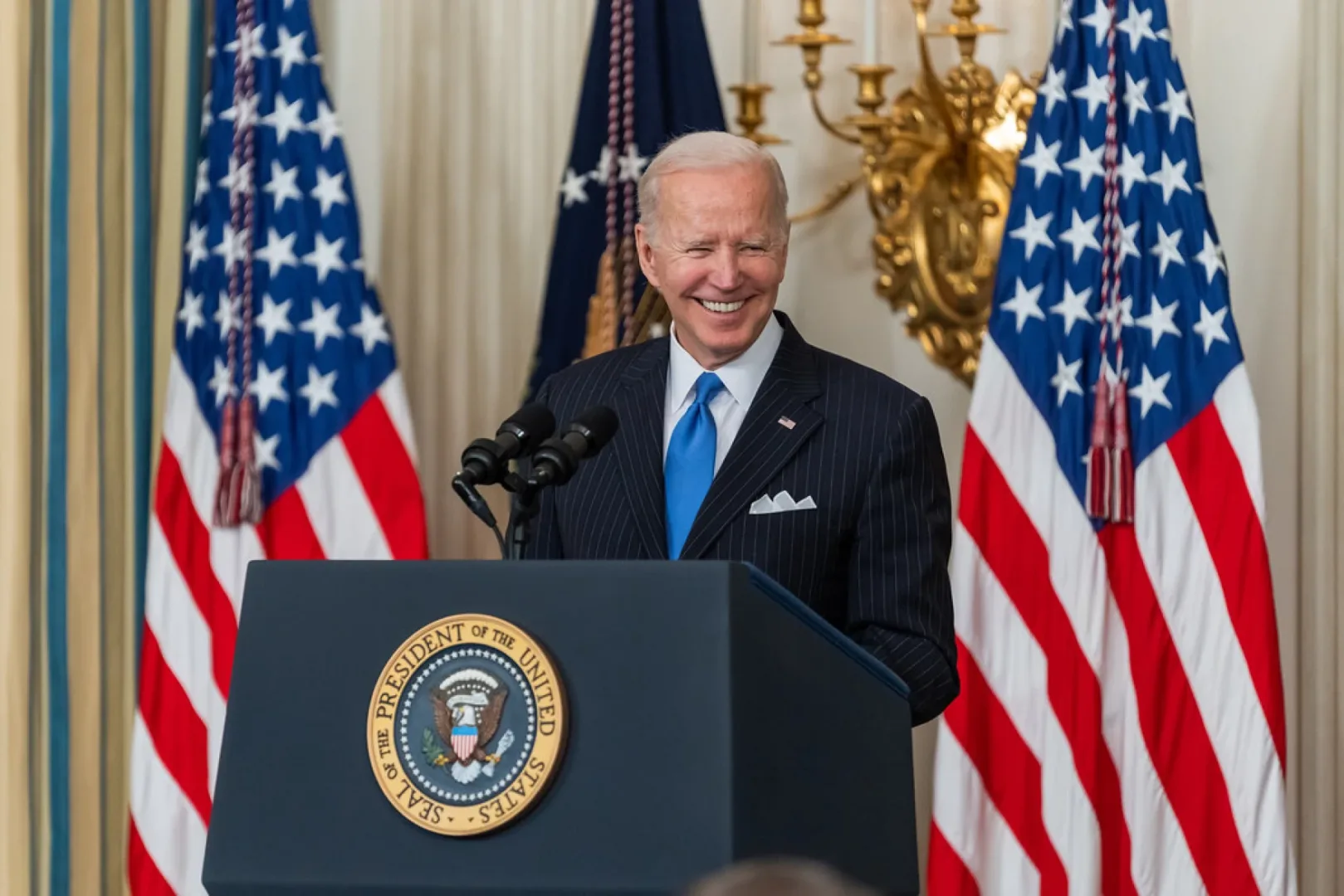 Biden smiles at a podium in front of two American flags.