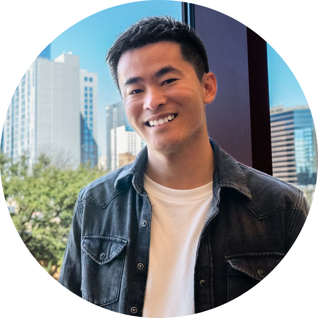 Justin Justin is an Asian American intersex person. He has short, dark hair and wears a jean jacket over a white t-shirt. He smiles widely in front of a city background of large buildings.